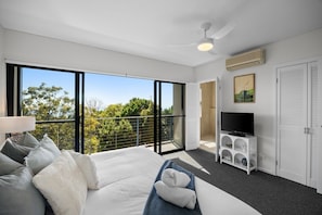 A modern bedroom with a large bed, a television, and a balcony with a view of trees. - Breathtaking whitewater views all the way to Noosa (Coolum Beach)