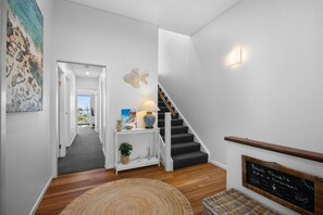 A hallway with a staircase, a console table with decorative items, a rug, and a chalkboard with beach towel information. - Breathtaking whitewater views all the way to Noosa (Coolum Beach)