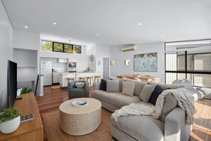 A modern living space with a sofa, coffee table, and a kitchen area in the background. - Breathtaking whitewater views all the way to Noosa (Coolum Beach)