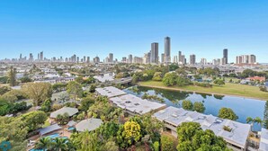 A residential area with houses, a lake, and a city skyline in the background. - Water Views at Pacific Keys Central - Hosted By Gold Coast Holiday Stays (Mermaid Waters)