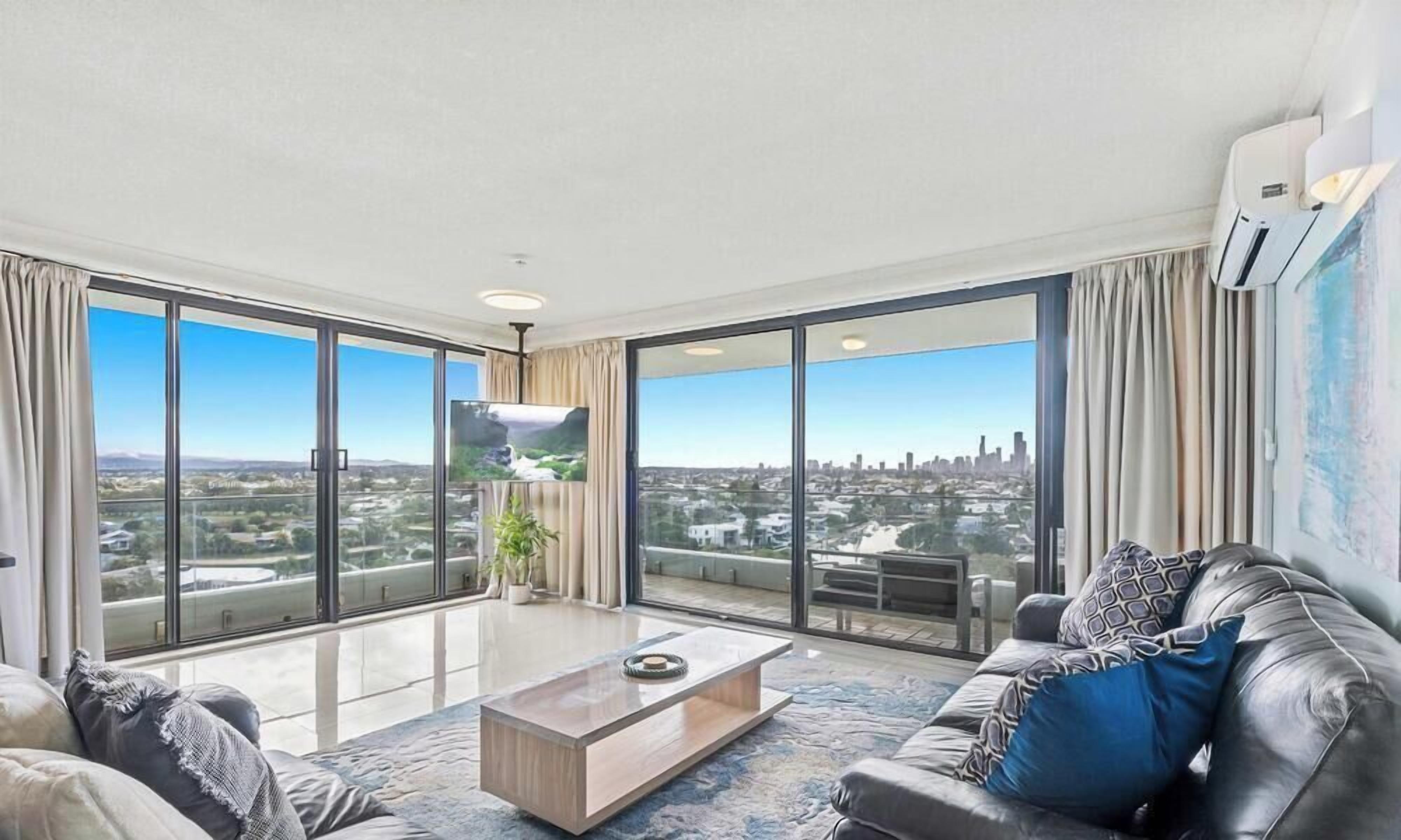 A modern living room with a large window, a flat-screen TV, and a leather sofa.