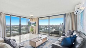 A modern living room with a large window, a flat-screen TV, and a leather sofa. - Water Views at Pacific Keys Central - Hosted By Gold Coast Holiday Stays (Mermaid Waters)