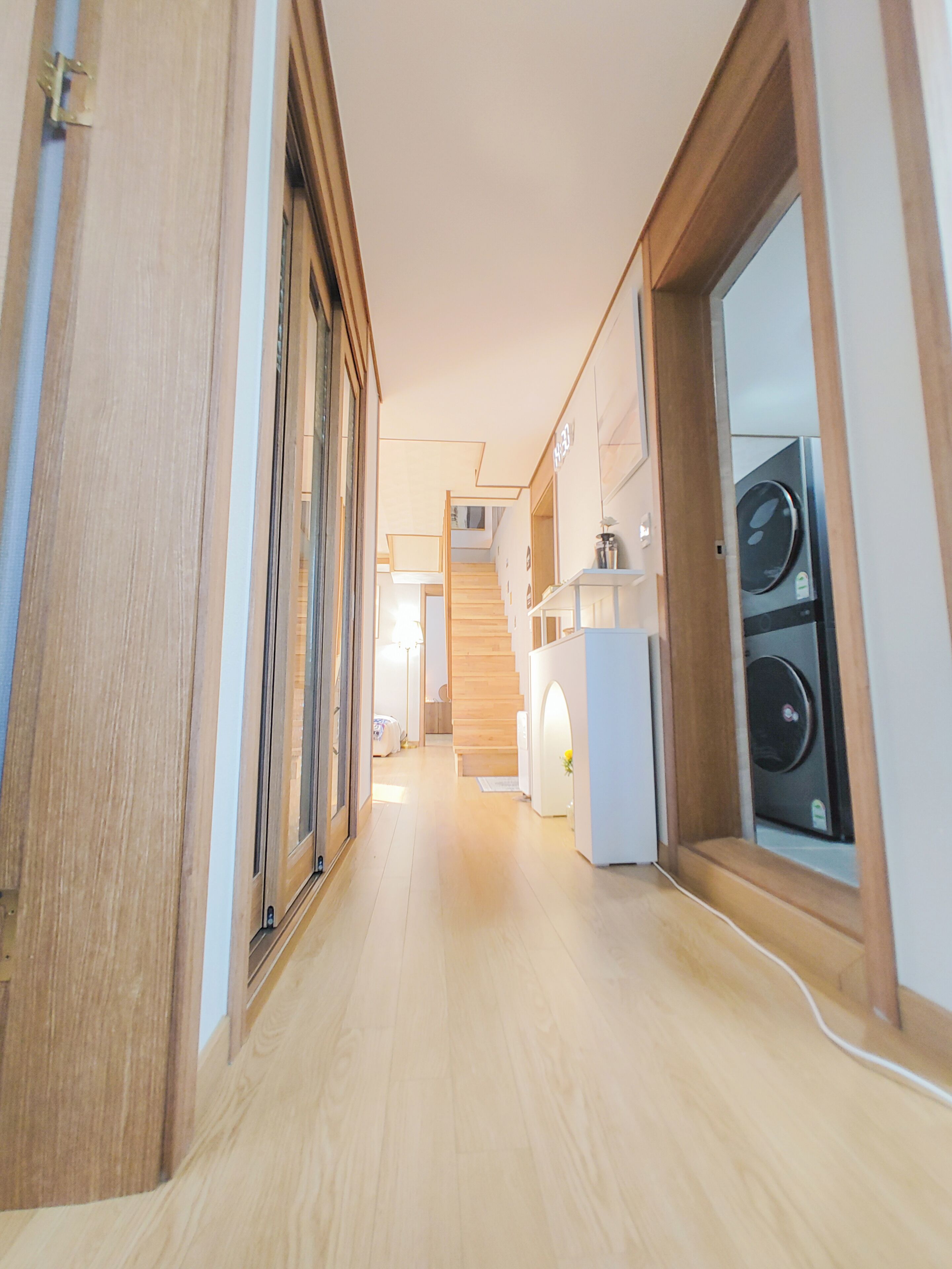 A hallway with wooden flooring, a staircase, and a laundry area with washing machines.