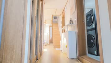 A hallway with wooden flooring, a staircase, and a laundry area with washing machines.