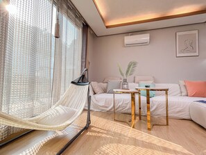 A modern living room with a hammock chair, a sofa, a coffee table, and a wall-mounted air conditioner.