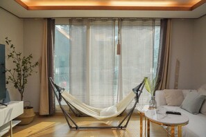 A room with a hammock chair, a sofa, a small table, and a potted plant.