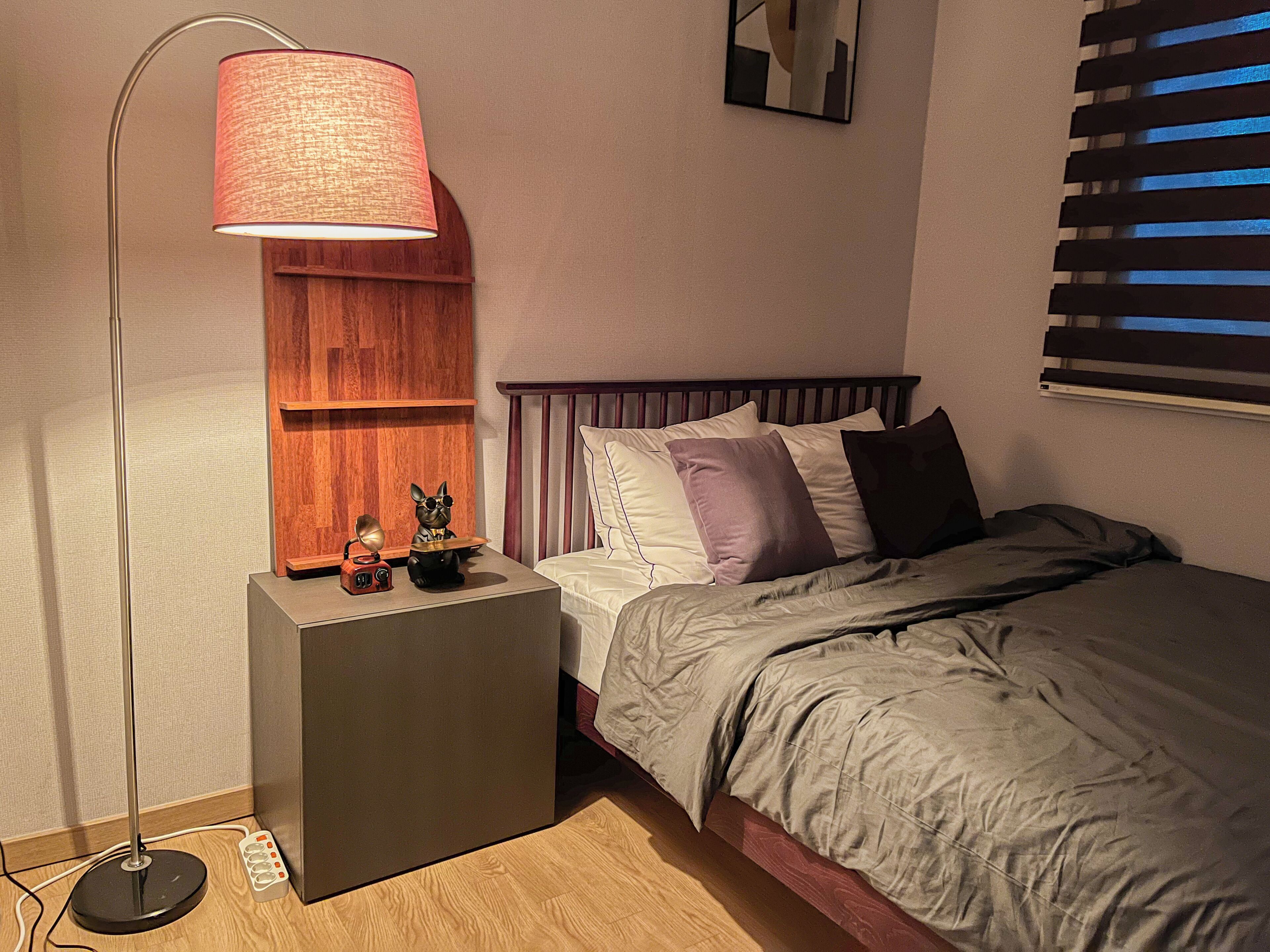 A bedroom with a bed, bedside table, lamp, and a wall-mounted mirror.
