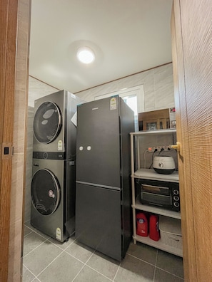 A compact kitchen with a Samsung refrigerator, a washing machine, a toaster, and a shelf with cleaning supplies. - Cozy Family House in the nature of Ganghwa Island with BBQ & Campfire (Ganghwa-gun)