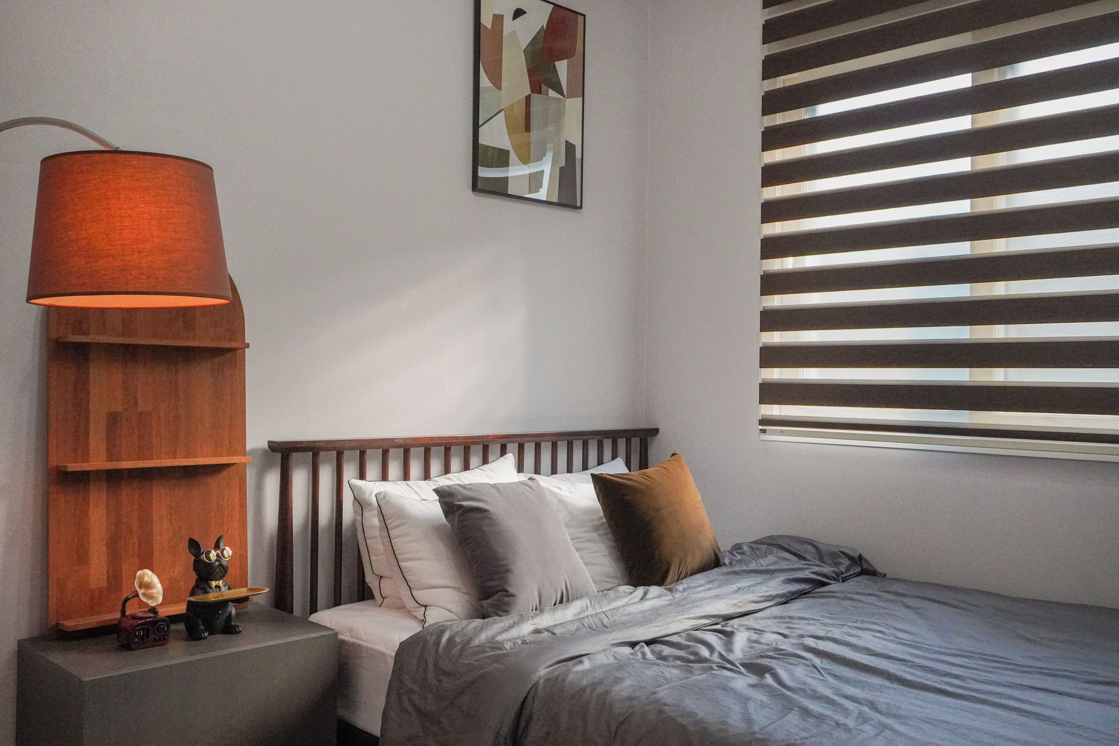 Un dormitorio con cama, mesita de noche, lámpara y ventana con persianas.