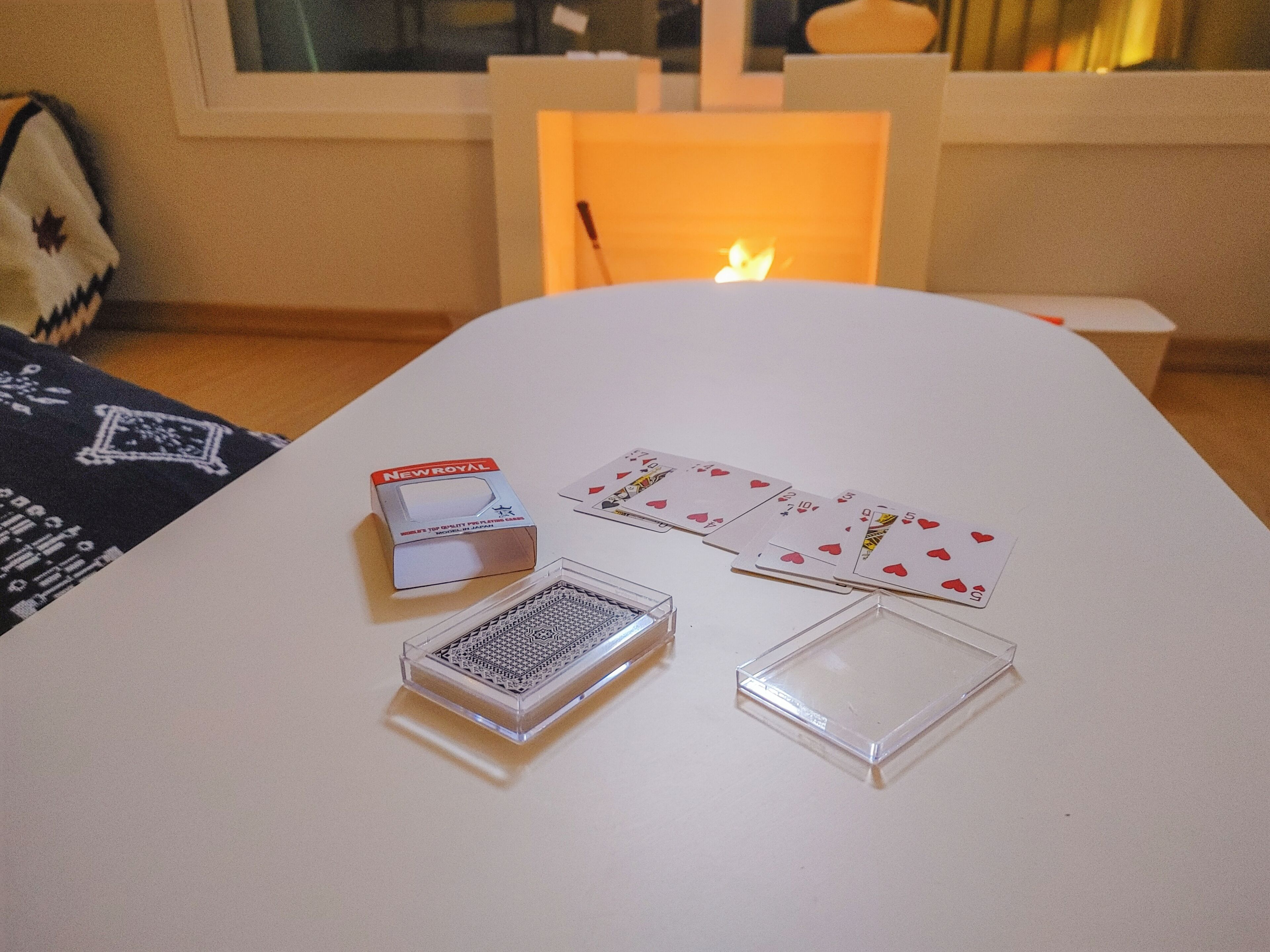 A white table with playing cards, a matchbox, and a candle.