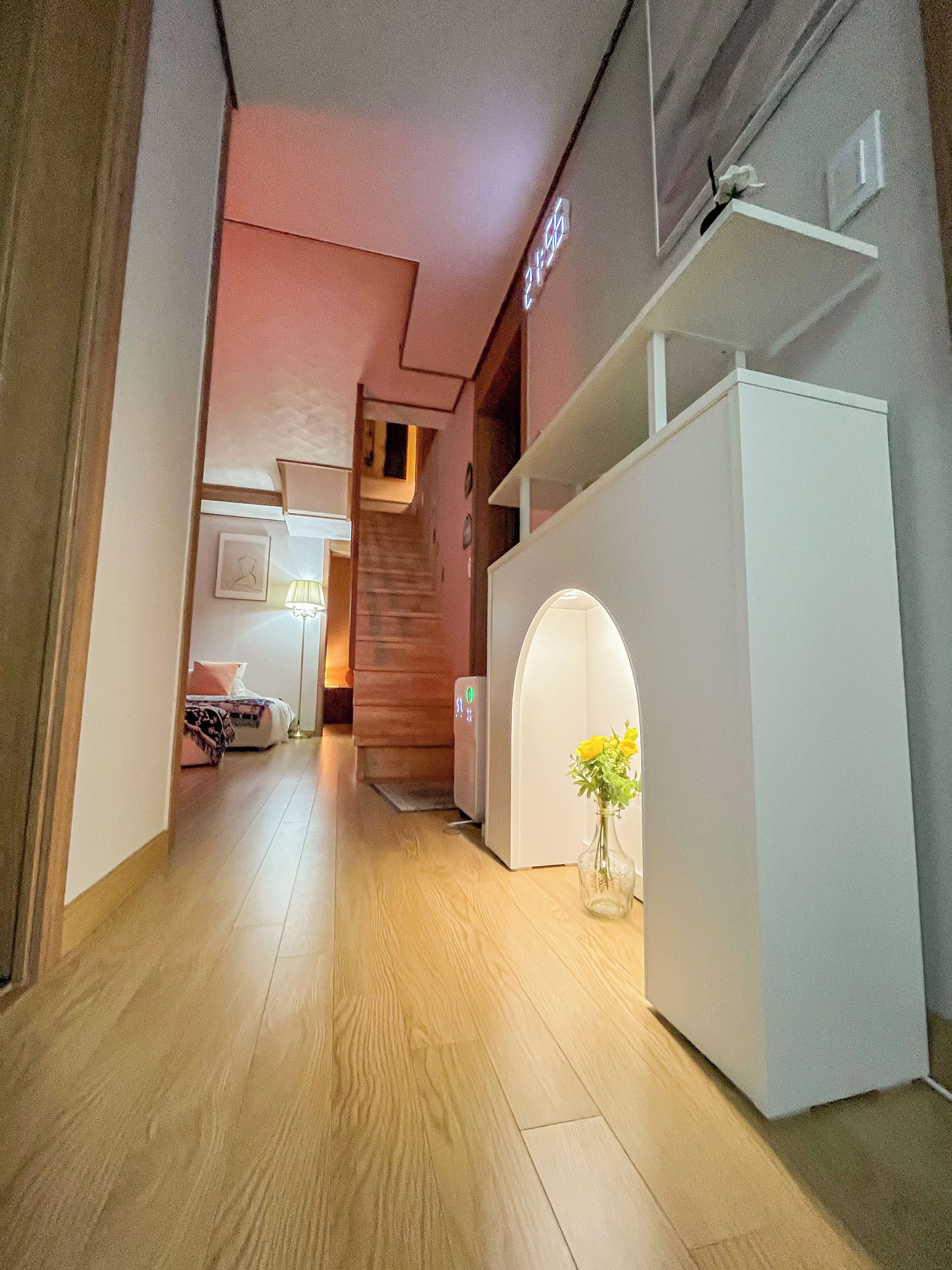 A hallway with a staircase, a bed, a white cabinet, and a vase with flowers.