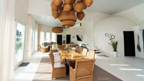 Een ruime woonruimte met een grote houten eettafel, rieten meubels en een trap naar een ander niveau.
