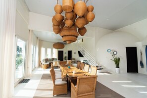 A spacious living area with a large wooden dining table, wicker furniture, and a staircase leading to another level.