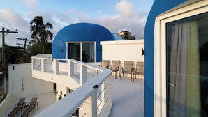 Een modern gebouw met een blauwe koepelstructuur, een balkon met stoelen en een heldere lucht.
