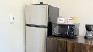 Una kitchenette con refrigerador de acero inoxidable, microondas y cafetera sobre un mueble de madera.