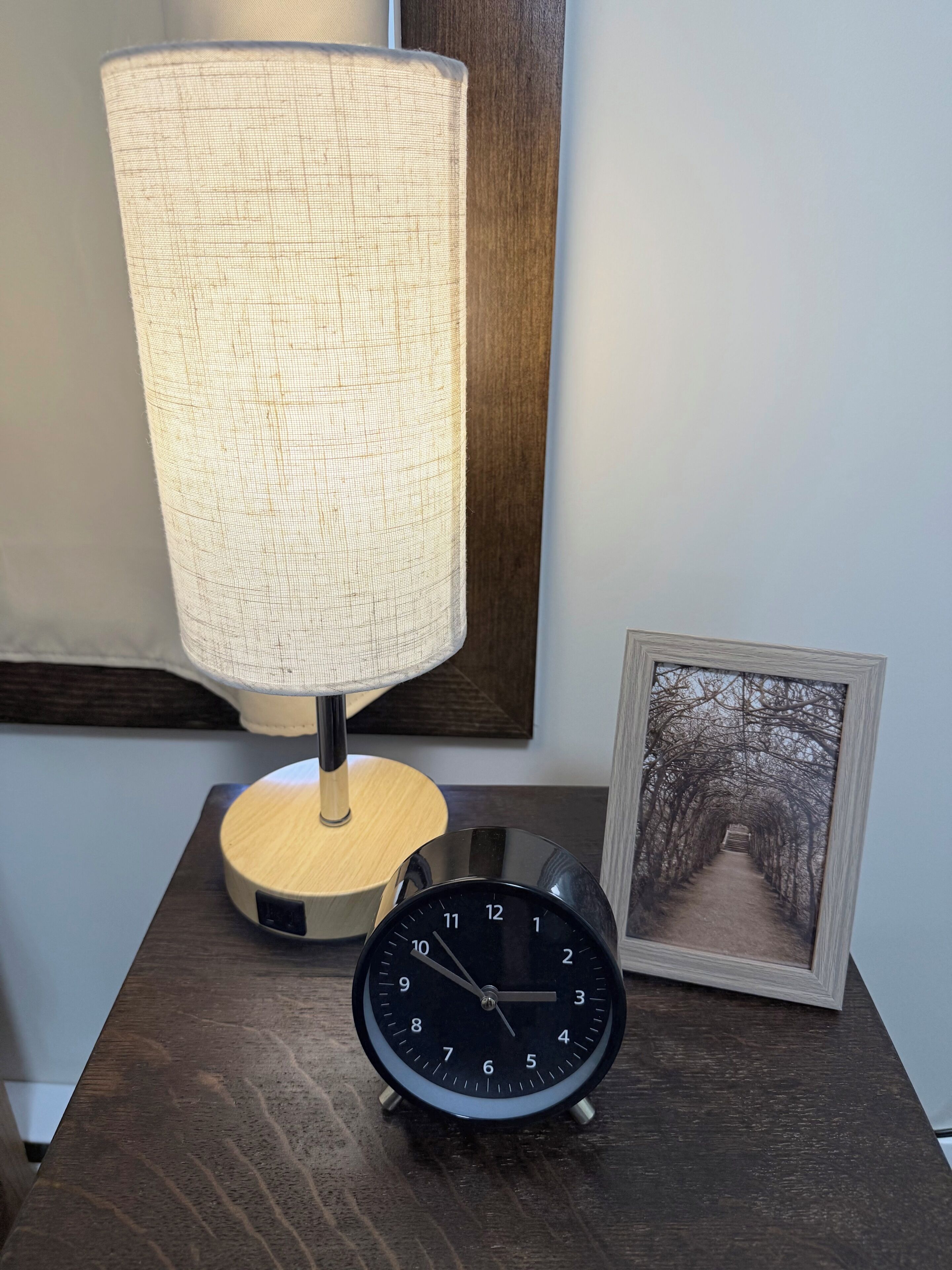A bedside table with a lamp, a clock, and a framed picture.