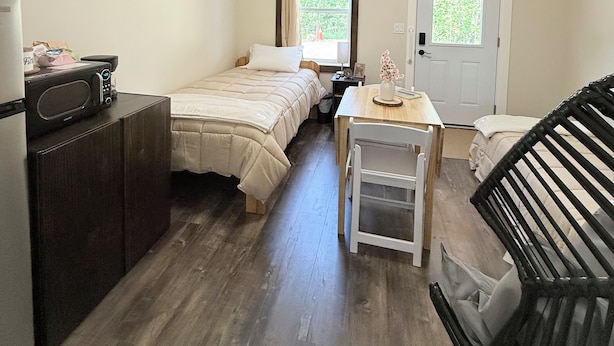 Habitación compacta con cama, una mesita, una silla, microondas y una puerta con ventana.