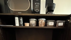 Una cocina con microondas, cafetera y varios recipientes en estantes.