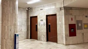 Un couloir aux murs de marbre et doté de deux portes en bois, dont l’une est surmontée d’une enseigne.