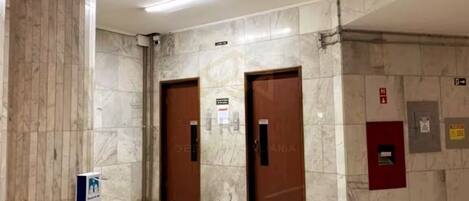 A hallway with marble walls and two wooden doors, one of which has a sign above it.