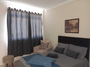 Une chambre à coucher avec un lit, une chaise, une table de chevet et un tableau au mur.