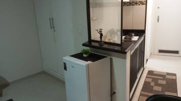 Uma cozinha compacta com geladeira, bancada pequena e um vaso com planta.