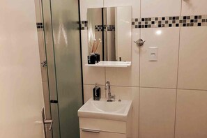 Un bany amb una cabina de dutxa de vidre, un lavabo blanc amb un mirall a sobre i una paret amb rajola i una franja decorativa.