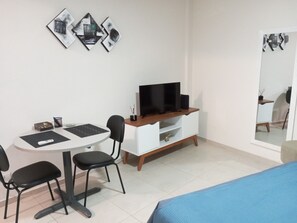 A hotel room with a bed, a desk with a chair, a television on a wooden stand, and a mirror on the wall.