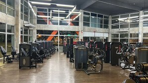 A gym with various exercise machines, large windows, and a high ceiling.