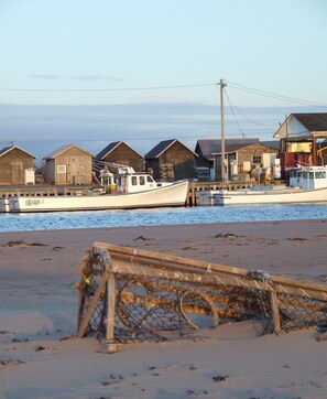 Et kystlandskab med en båd ved et piblad, en sandstrand og fiskeredskaber.