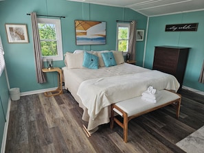 A bedroom with a large bed, bedside tables, a bench, and a wardrobe. - Lyons Cottages - #7 King Studio Walk to the Beaches of Stanhope National Park! (Stanhope)