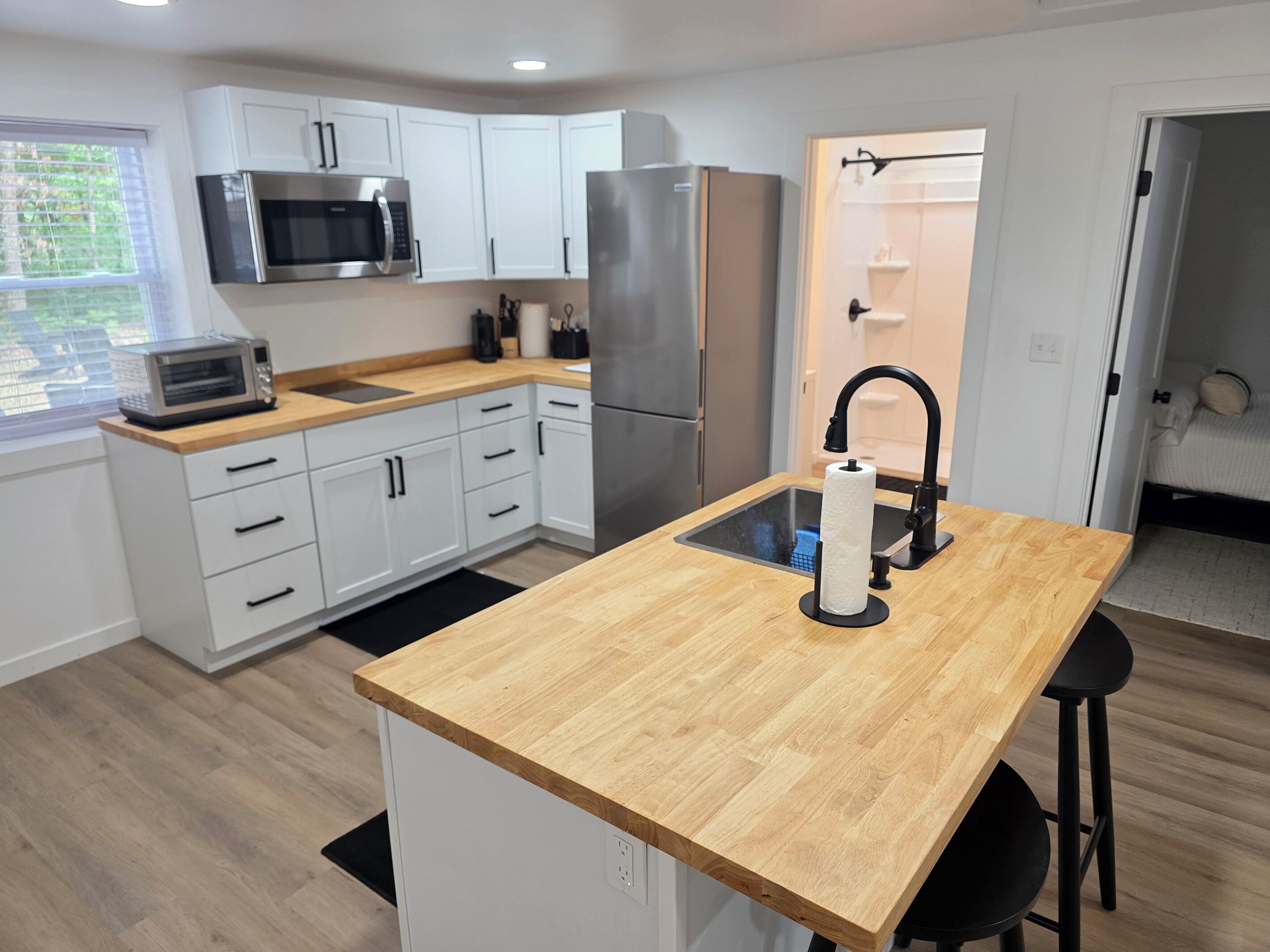 A modern kitchen with white cabinets, stainless steel appliances, a wooden countertop island, and a black faucet.