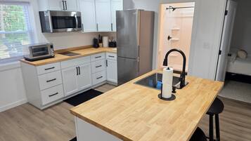A modern kitchen with white cabinets, stainless steel appliances, a wooden countertop island, and a black faucet.