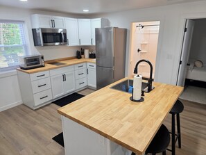 A modern kitchen with white cabinets, stainless steel appliances, a wooden countertop island, and a black faucet. - The Haven at Idlewild (Idlewild)