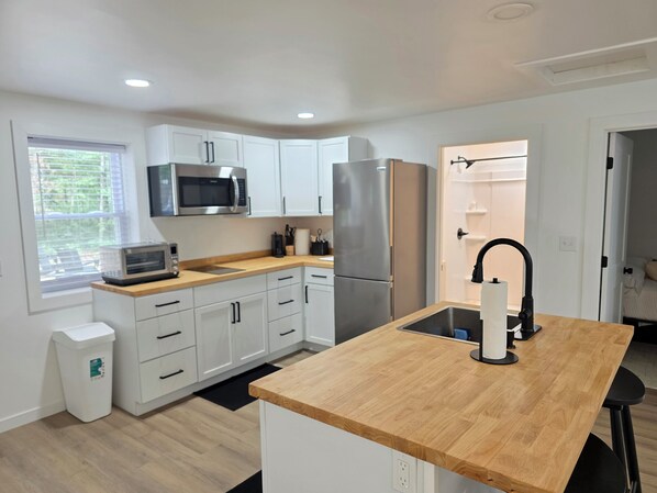 A modern kitchen with white cabinets, stainless steel appliances, a wooden countertop, and a black faucet.
