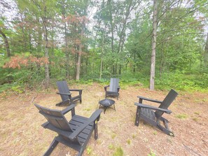An outdoor seating area with Adirondack chairs and a fire pit surrounded by a forest.