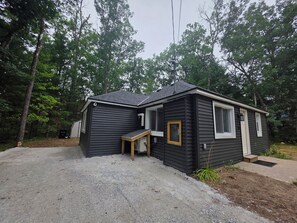 A small, dark-colored cabin with a gravel driveway, surrounded by trees. - The Haven at Idlewild (Idlewild)