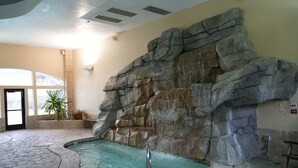 Ein Poolbereich im Innenbereich mit einer Felswand, einem Whirlpool und einem gefliesten Boden.