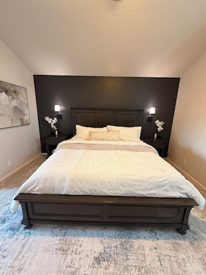A bedroom with a large bed, dark headboard, two bedside lamps, and a wall-mounted artwork. - The Main Event: Theater • Hot Tub • GameDay Retreat • Near Autzen• Fi... (Eugene)