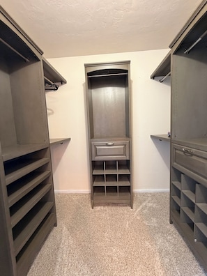 Un dressing accessible sans porte, doté d’étagères ouvertes, d’un meuble à tiroirs central et d’une tringle pour suspendre les vêtements.