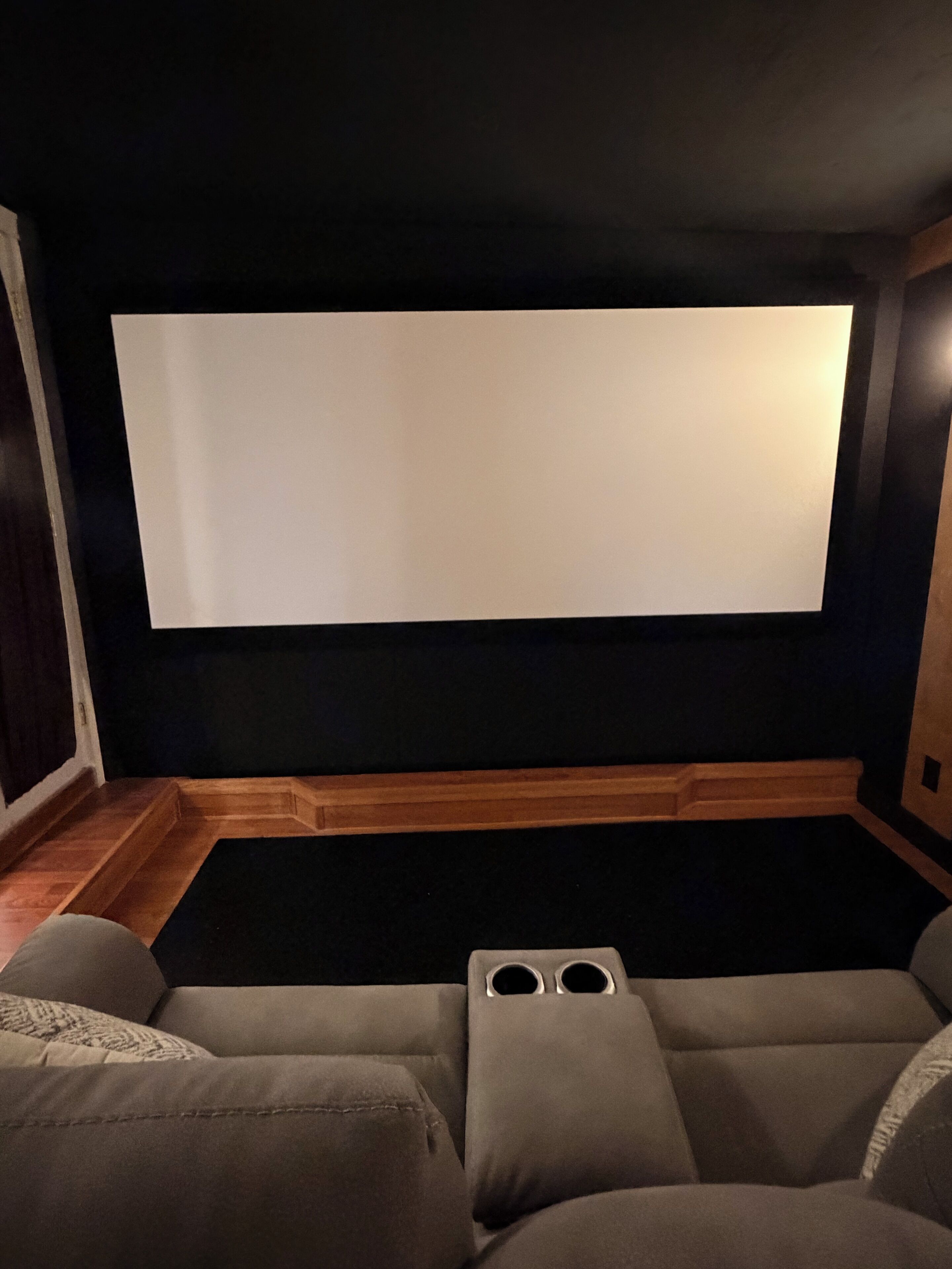 Ein Heimkinozimmer mit großer Leinwand, Holzvertäfelung und einem Ecksofa.