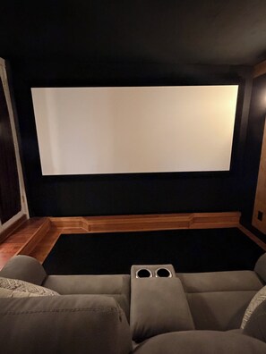 A home theater room with a large screen, wooden paneling, and a sectional sofa. - The Main Event: Theater • Hot Tub • GameDay Retreat • Near Autzen• Fi... (Eugene)