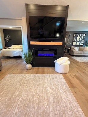 A modern living room with a flat-screen TV, a fireplace with a blue-lit lower section, a sofa, a coffee table, and a potted plant. - The Main Event: Theater • Hot Tub • GameDay Retreat • Near Autzen• Fi... (Eugene)