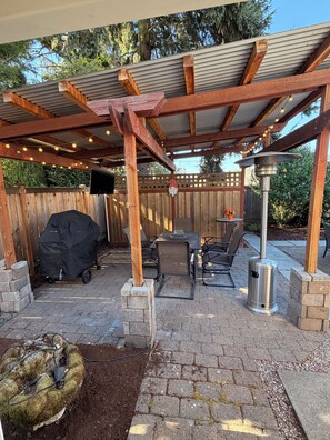 En uteplats med en pergola, en grill och ett bord med stolar.