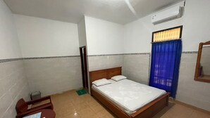 A room with a bed, a wooden nightstand, a mirror, and a window with blue curtains. - OYO 95369 Hotel Sari Mandala (Negara)