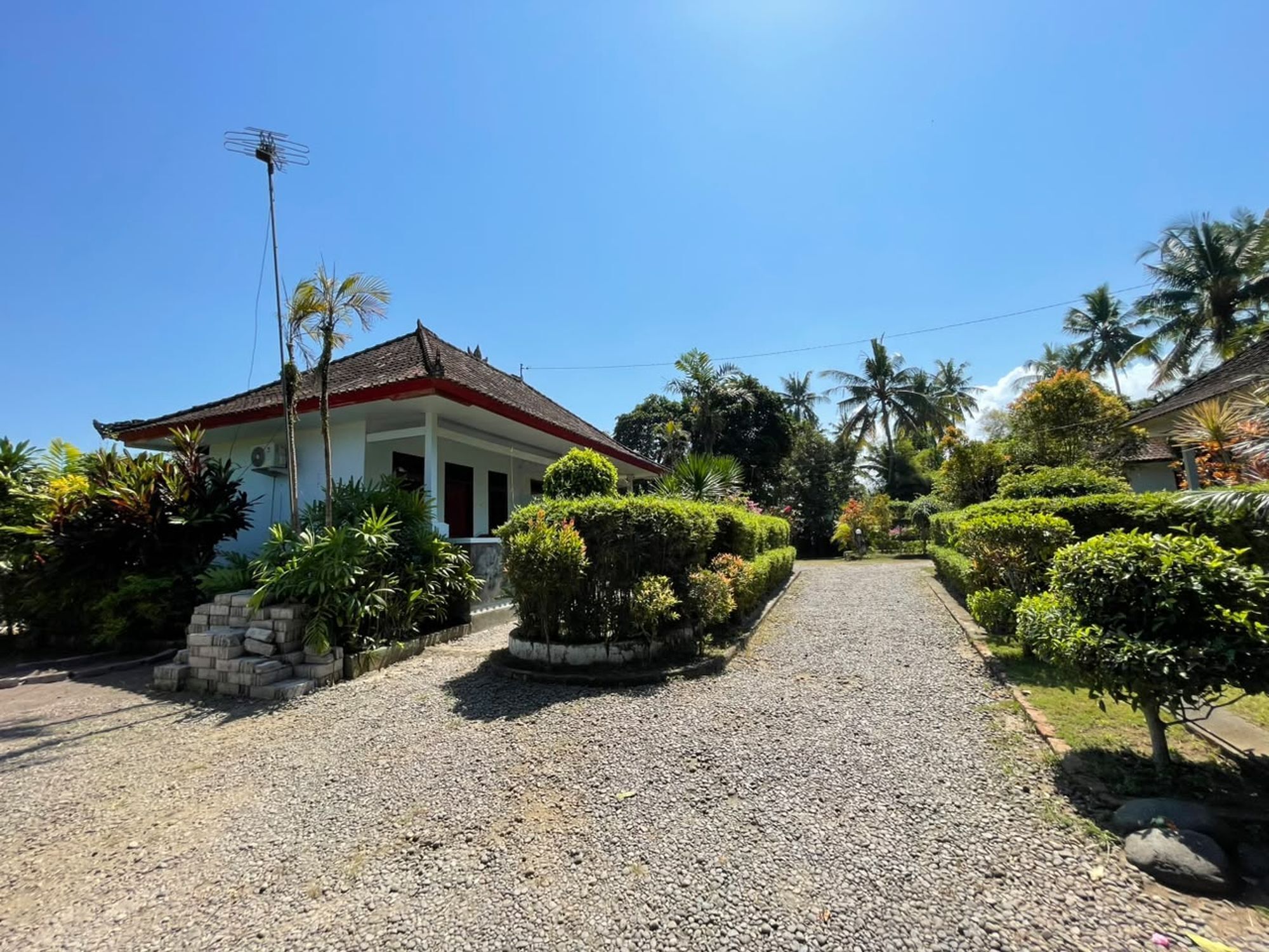 A house with a gravel driveway, surrounded by well-maintained gardens and palm trees.
