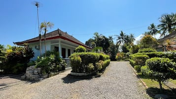 Una casa con entrada de grava, rodeada de jardines cuidados y palmeras.