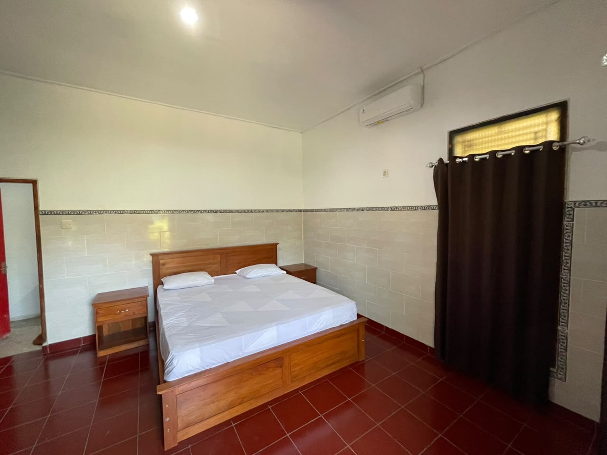 A bedroom with a wooden bed, a nightstand, a mirror, and a window with curtains.
