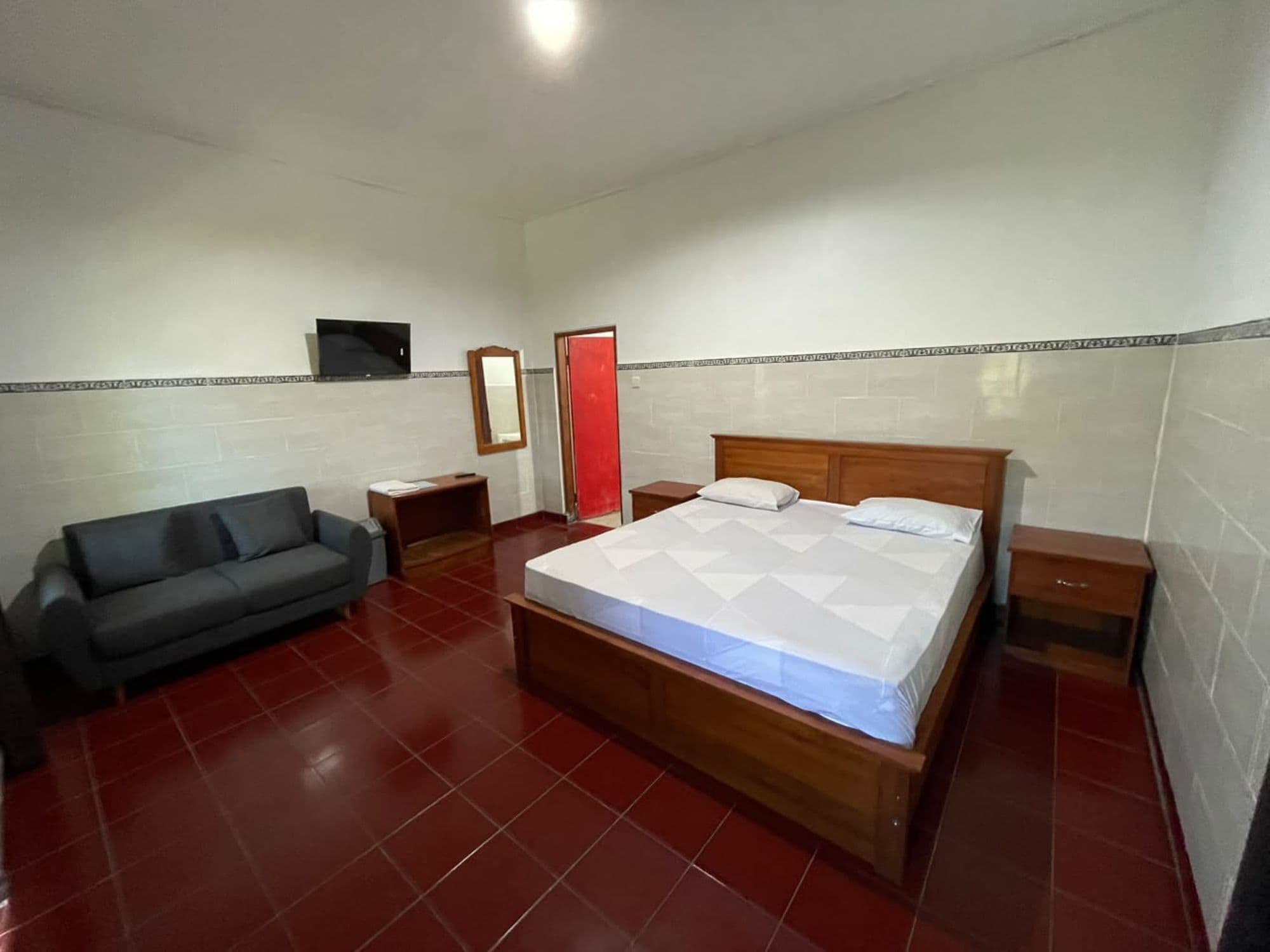 Un dormitorio con cama, sofá, televisión y espejo.