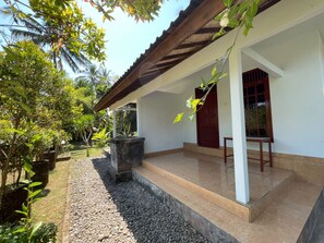 A covered outdoor area with a tiled floor, a concrete planter, and a wooden table. - OYO 95369 Hotel Sari Mandala (Negara)